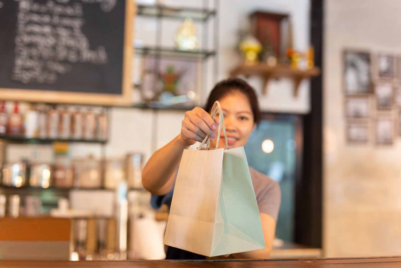 waitress at counter giving eco friendly paper bag with take away drink in cafe.